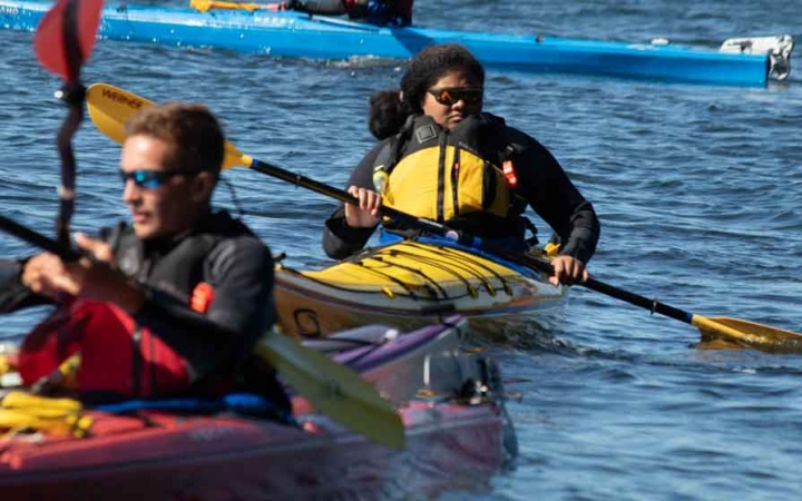 two kayakers paddle on blue water on an outward bound course for teens